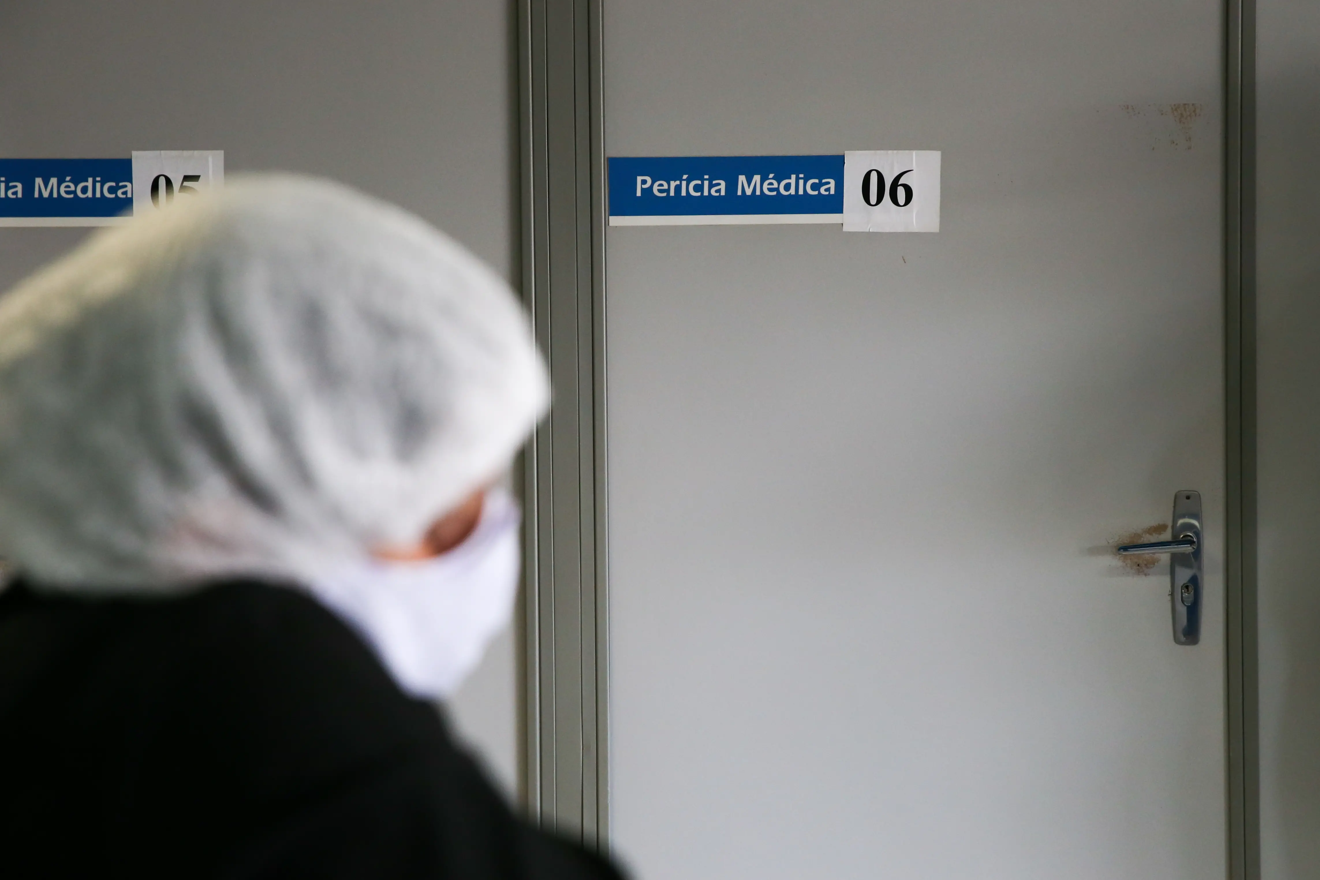 Profissional de costas, parada em frente a uma porta de uma sala que realiza perícia médica.