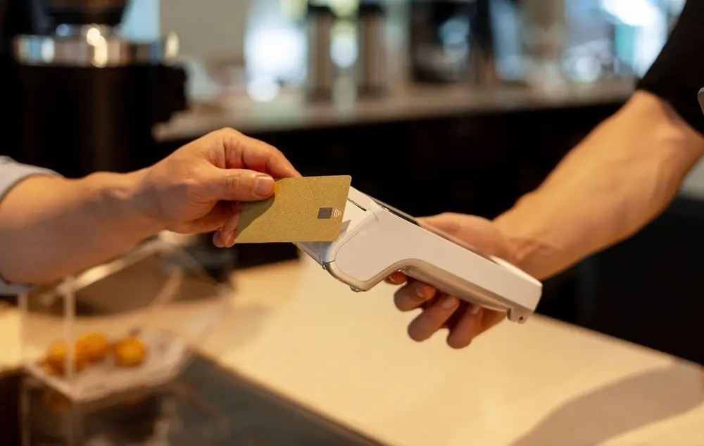 Sem mostrar rostos, cliente passa cartão em maquininha de estabelecimento comercial.