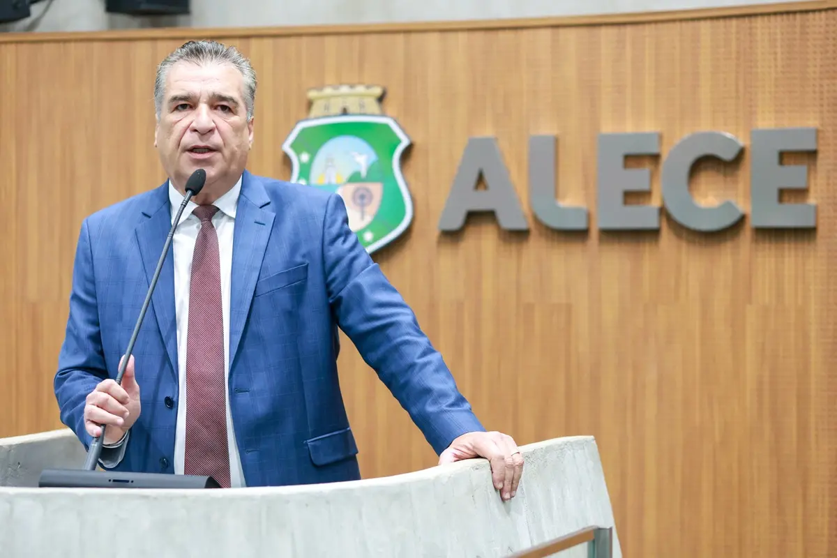 Homem de terno azul e gravata fala ao microfone em tribuna, com o brasão do Ceará e a palavra ‘ALECE’ ao fundo.