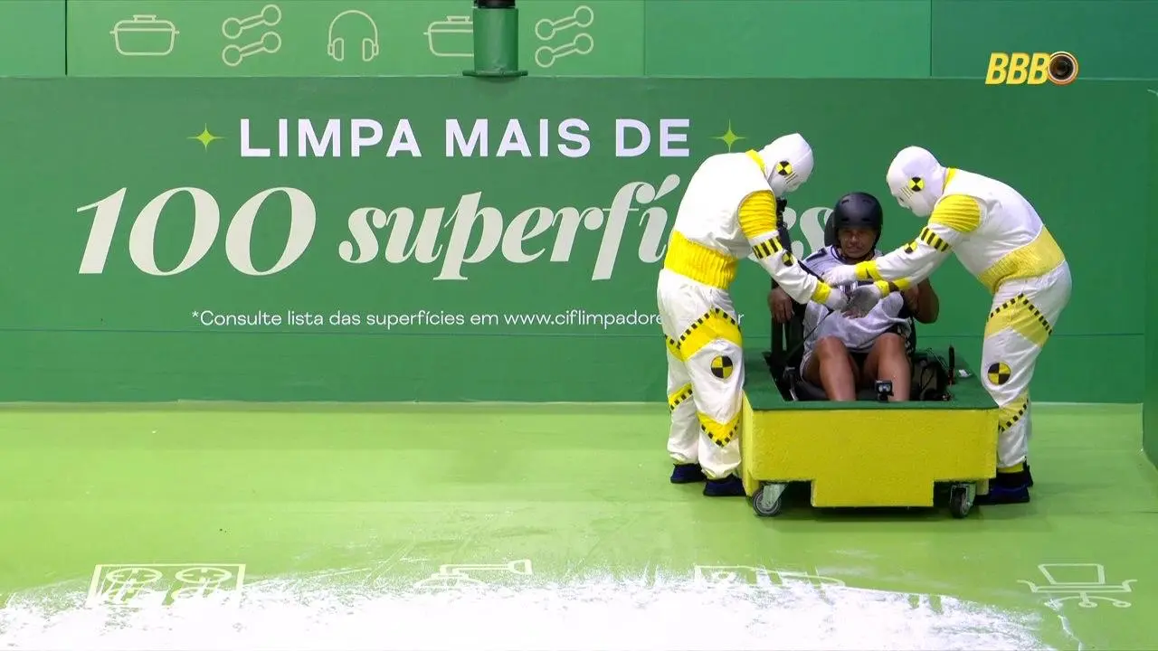 Cenário verde com texto promocional ao fundo; duas pessoas com macacões brancos e amarelos empurram um carrinho onde outra pessoa está sentada, em ação de demonstração de limpeza.