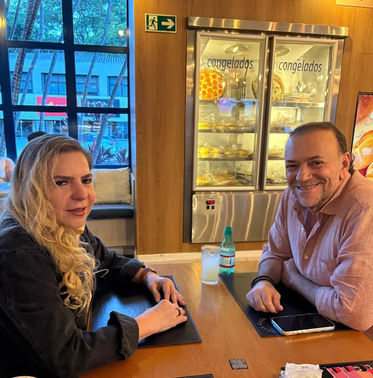 Luizianne Lins e Edinho durante conversa. Eles estão sentados à mesa e sorriem para a foto.