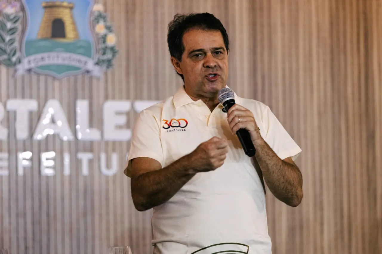 Prefeito Evandro Leitão fala com microfone e vestido com blusa de gola polo com o número 300 escrito na altura do ombro.