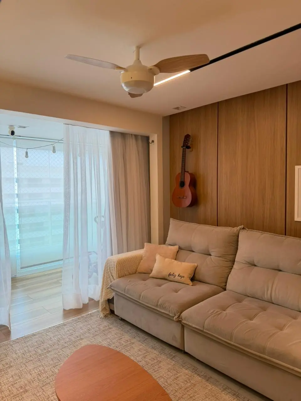 imagem de sala com sofá em destaque e cortina ao fundo. na parede, um violão está pendurado.