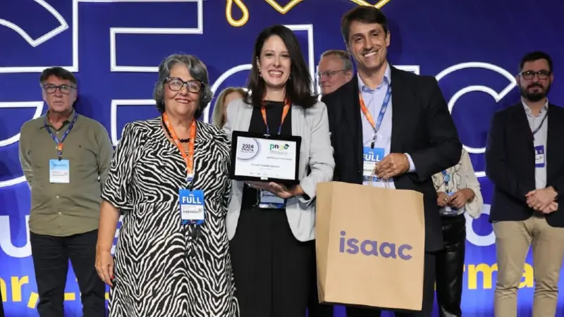 Equipe de profissionais celebrando uma conquista em evento de sustentabilidade, com destaque para uma mulher recebendo prêmio e sorrindo para a câmera.