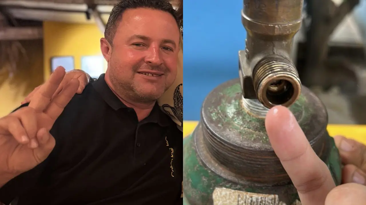 Close em uma válvula metálica rosqueada acoplada a um reservatório, com sinais de desgaste e oxidação. Um dedo aponta para a abertura da válvula, indicando o interior da conexão. O fundo é desfocado, sugerindo ambiente industrial ou técnico.