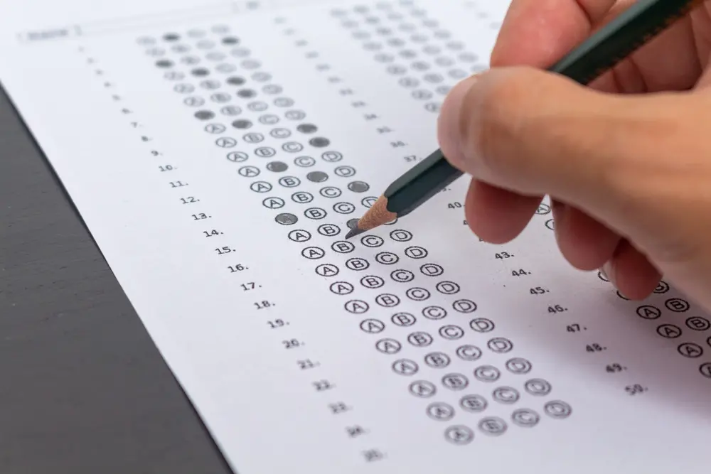 Pessoa preenchendo uma folha de resposta de múltipla escolha, foco em um exame ou teste de avaliação