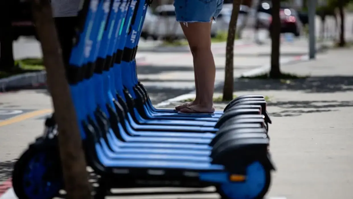 patinetes alinhados lado a lado. ao fundo, uma pessoa em cima de um dos equipamentos.