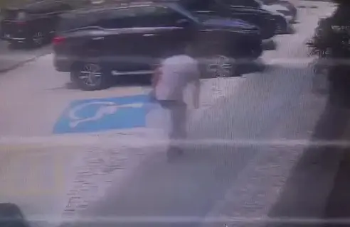 Foto que contém homem baleado. Ele está de branco e calça jeans, de costas e curvado para frente.