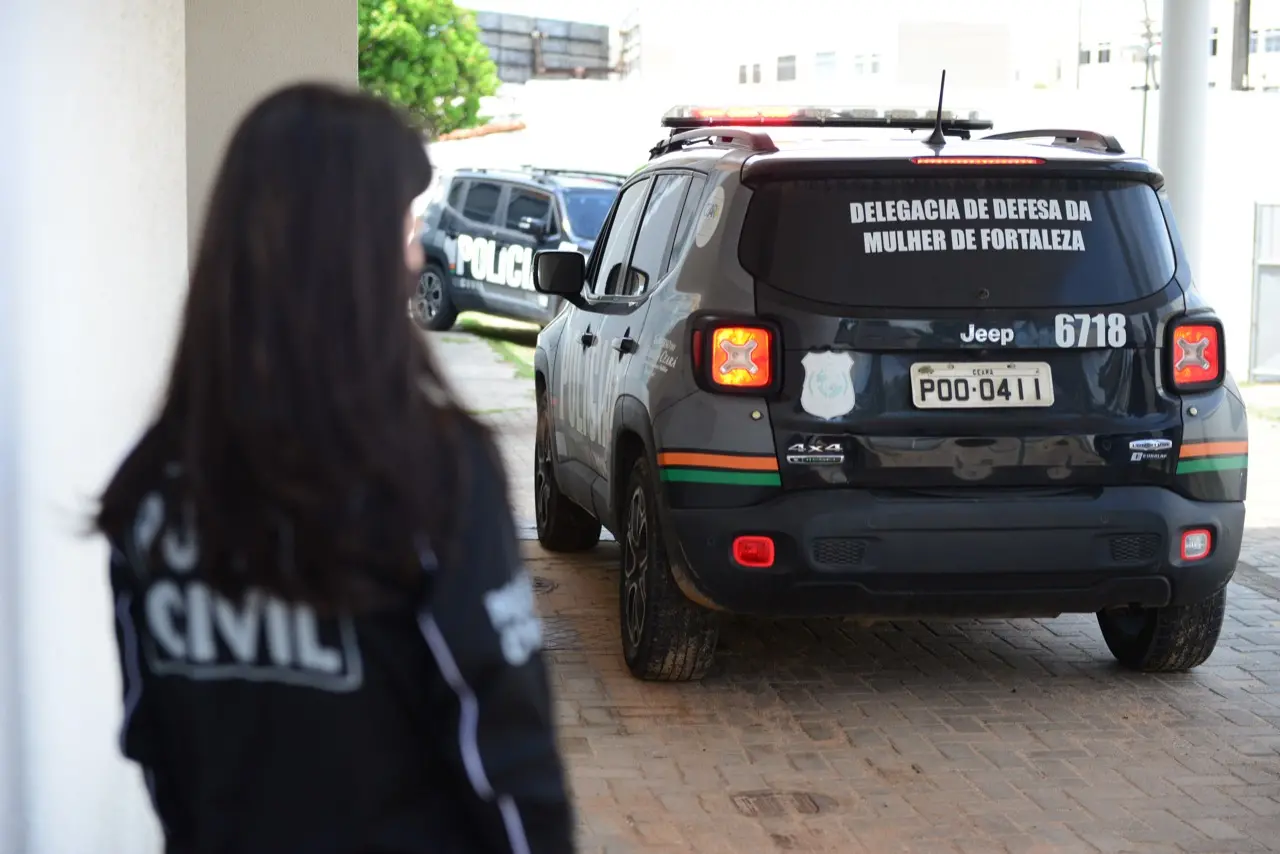 Viatura da Delegacia de Defesa da Mulher de Fortaleza estacionada em prédio oficial, com agente da Polícia Civil ao fundo.