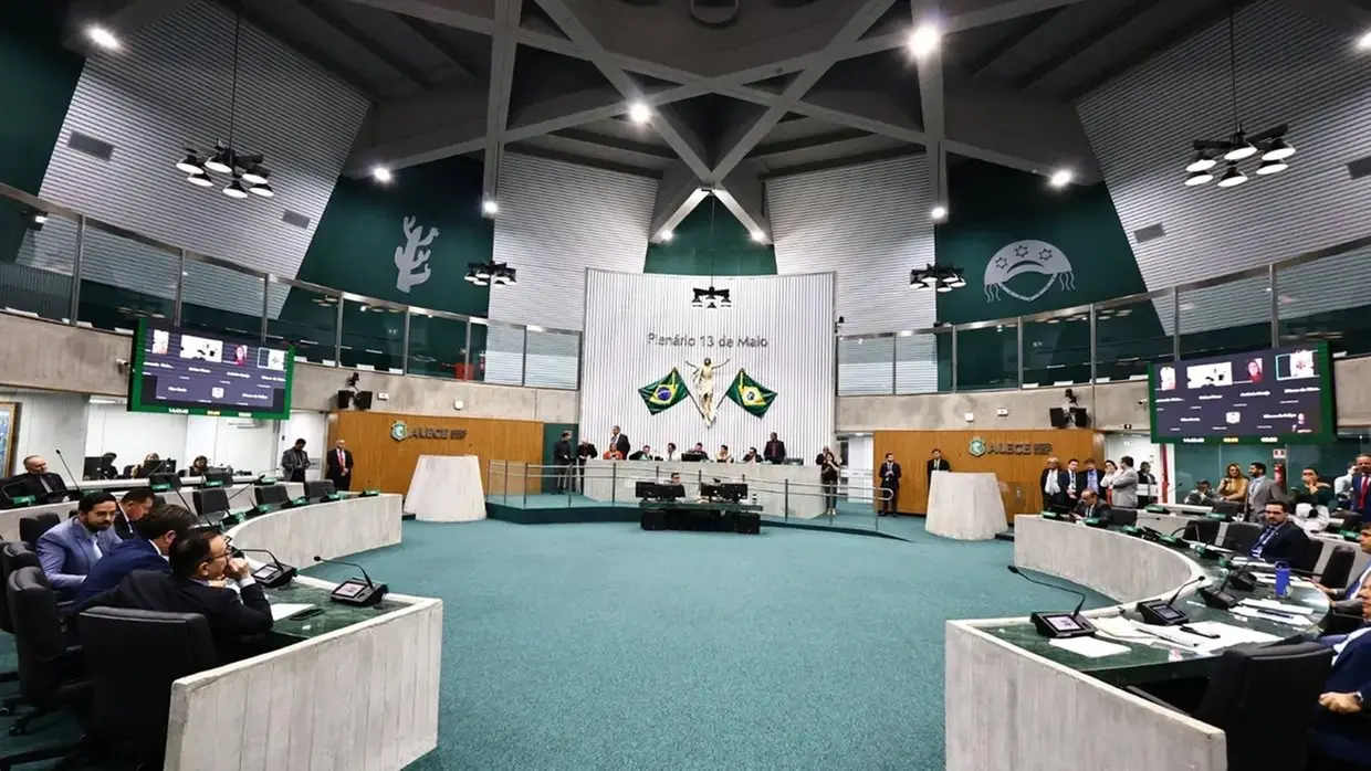 Plenário da Assembleia Legislativa do Ceará com deputados sentados em bancadas semicirculares, painel eletrônico ligado e bandeiras ao fundo durante sessão.