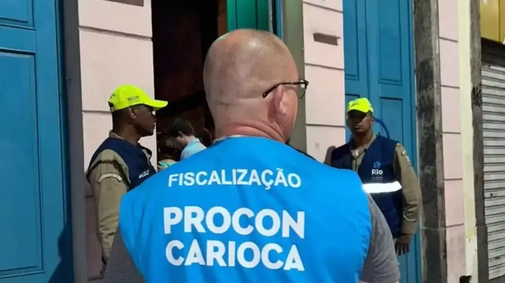 Na imagem, fotografia em plano médio mostrando as costas de um fiscal vestindo um colete azul claro com a inscrição 