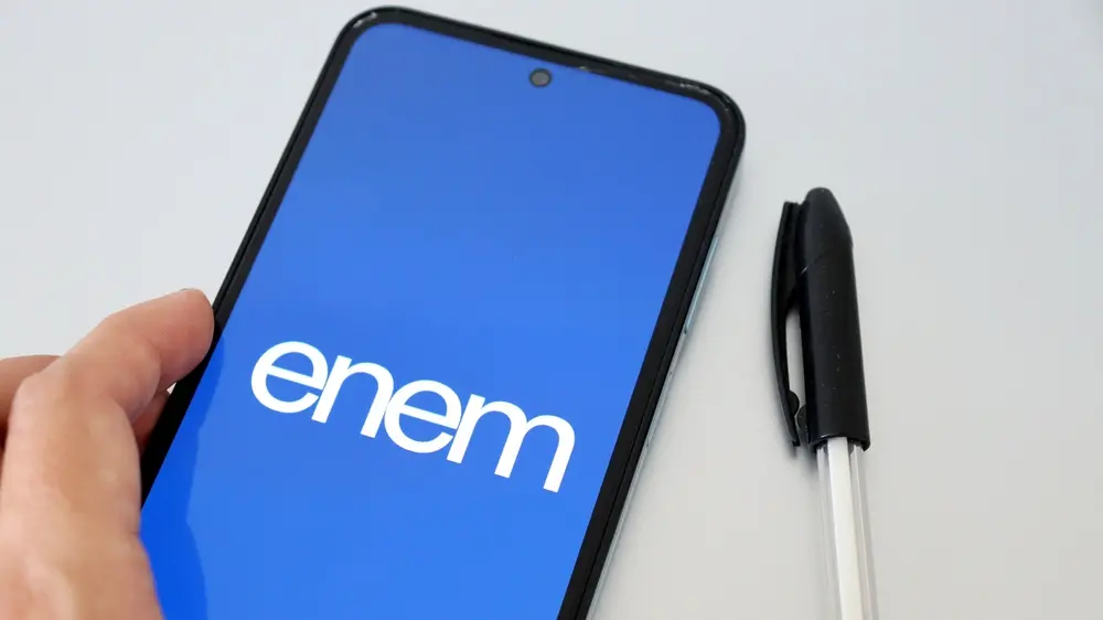 Imagem de um smartphone com a tela exibindo o logo da plataforma Enem, ao lado de uma caneta preta, simbolizando preparação para o exame.