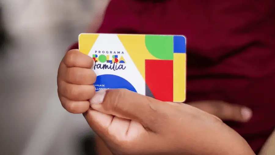 Pessoa segurando um cartão do programa Bolsa Família com cores vibrantes e design colorido.