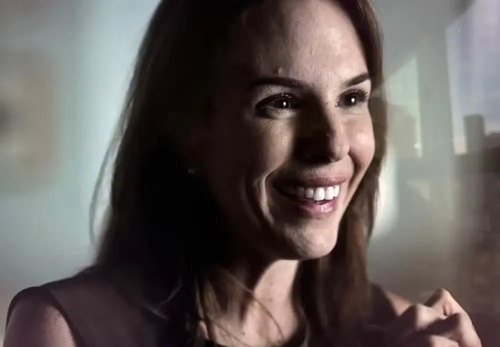 Mulher sorridente olhando pela janela, expressão de felicidade em rosto alegre.