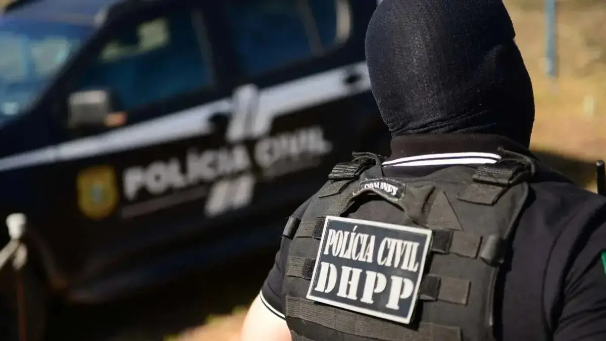 policial de costas, encapuzado, dhpp, policia civil, viatura ao fundo.