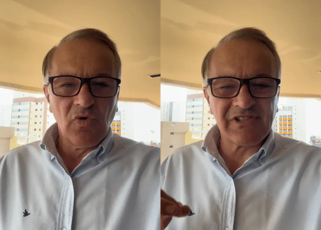 Imagem composta por duas fotos lado a lado do mesmo homem, em um ambiente externo, possivelmente uma varanda de apartamento. Ele aparenta ser um homem de meia-idade a idoso, com cabelo curto grisalho, usando óculos de armação escura e uma camisa branca de botão com um pequeno logotipo no peito.

Na primeira imagem (à esquerda), ele está com a boca levemente aberta, como se estivesse falando. Na segunda (à direita), aparece em posição semelhante, também falando, com a mão parcialmente levantada no primeiro plano, sugerindo gesticulação.

Ao fundo, há prédios residenciais de vários andares e uma iluminação natural suave, indicando que a cena ocorre durante o dia.