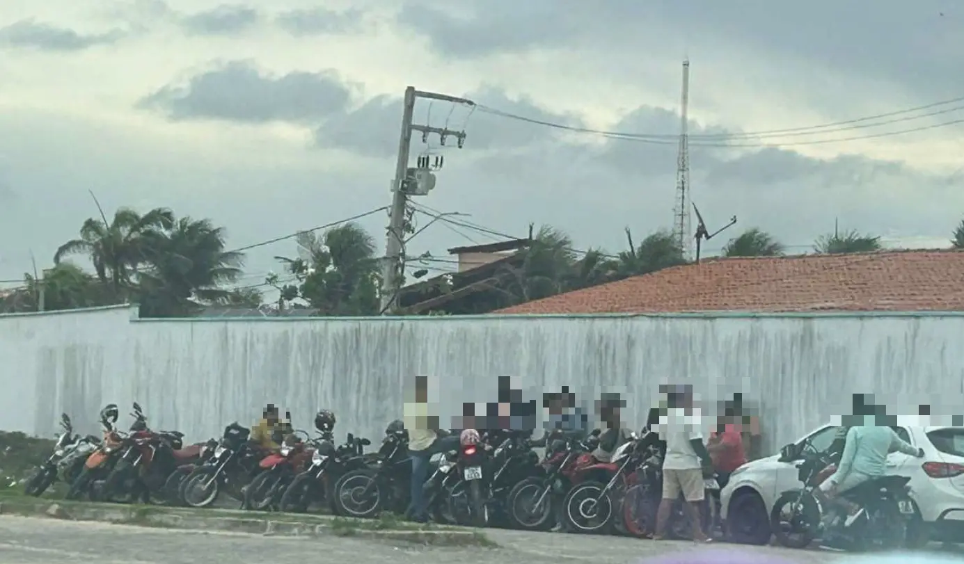 Foto que mostra diversas motocicletas e um carro estacionados em uma rua de Aquiraz, na Região Metropolitana de Fortaleza. Ao lado dos veículos estão motociclistas e motoristas de aplicativo.