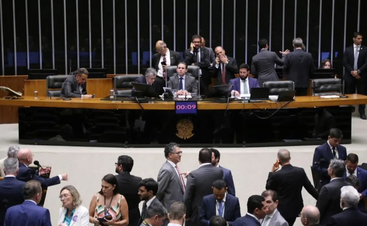 Sessão na Câmara dos Deputados, com vários parlamentares em pé perto de mesa central.