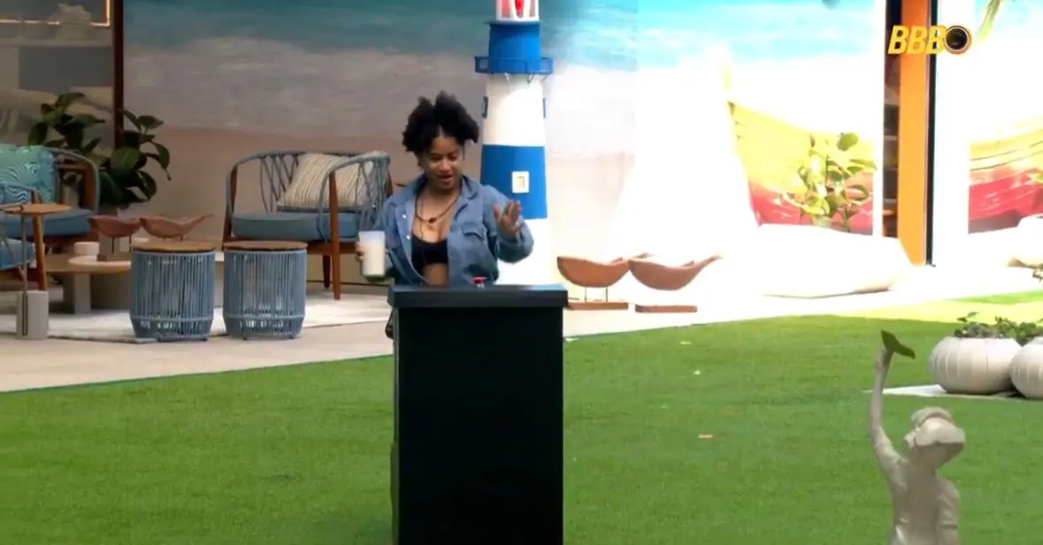 Milena apertando botão em totem colocado no gramado da casa do BBB 26.