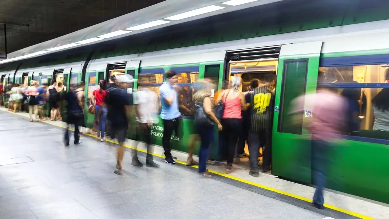 Imagem borrada de passageiros entrando e saindo de metrô em Fortaleza.