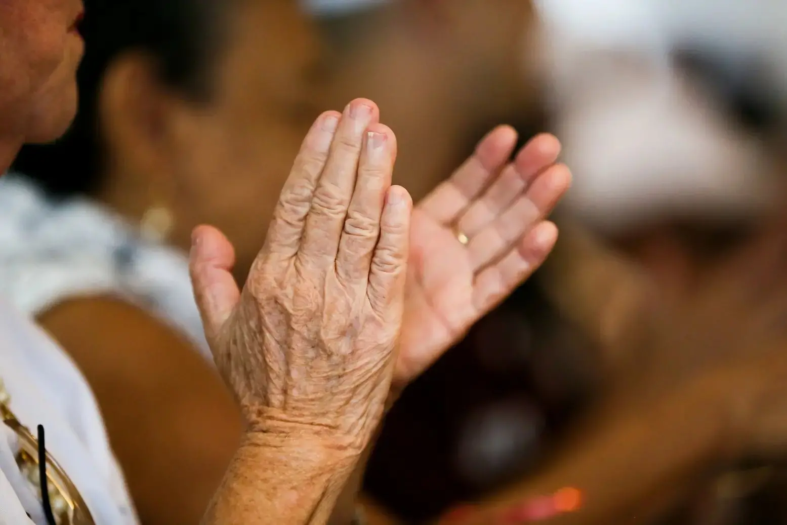 Imagem mostra close-up em mãos de mulher idosa em movimento de bater palmas.
