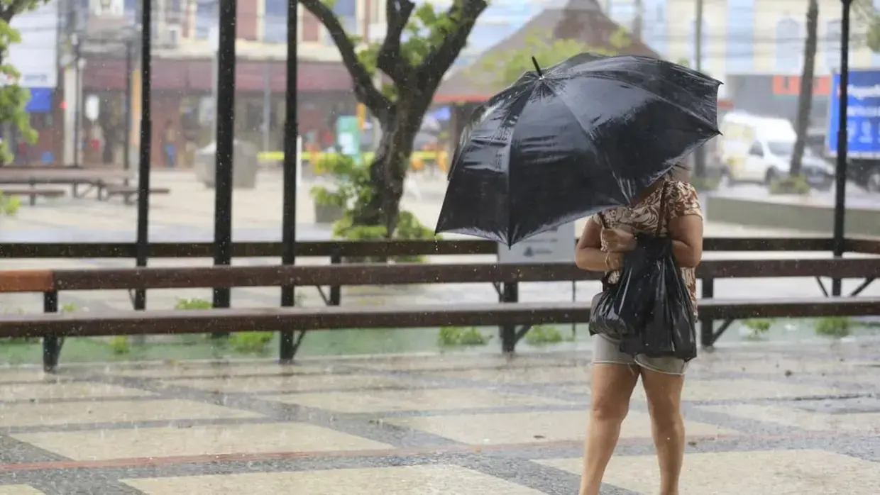 Mulher caminha sozinha usando guarda-chuva preto em dia chuvoso na Praça do Ferreira, no Centro de Fortaleza.