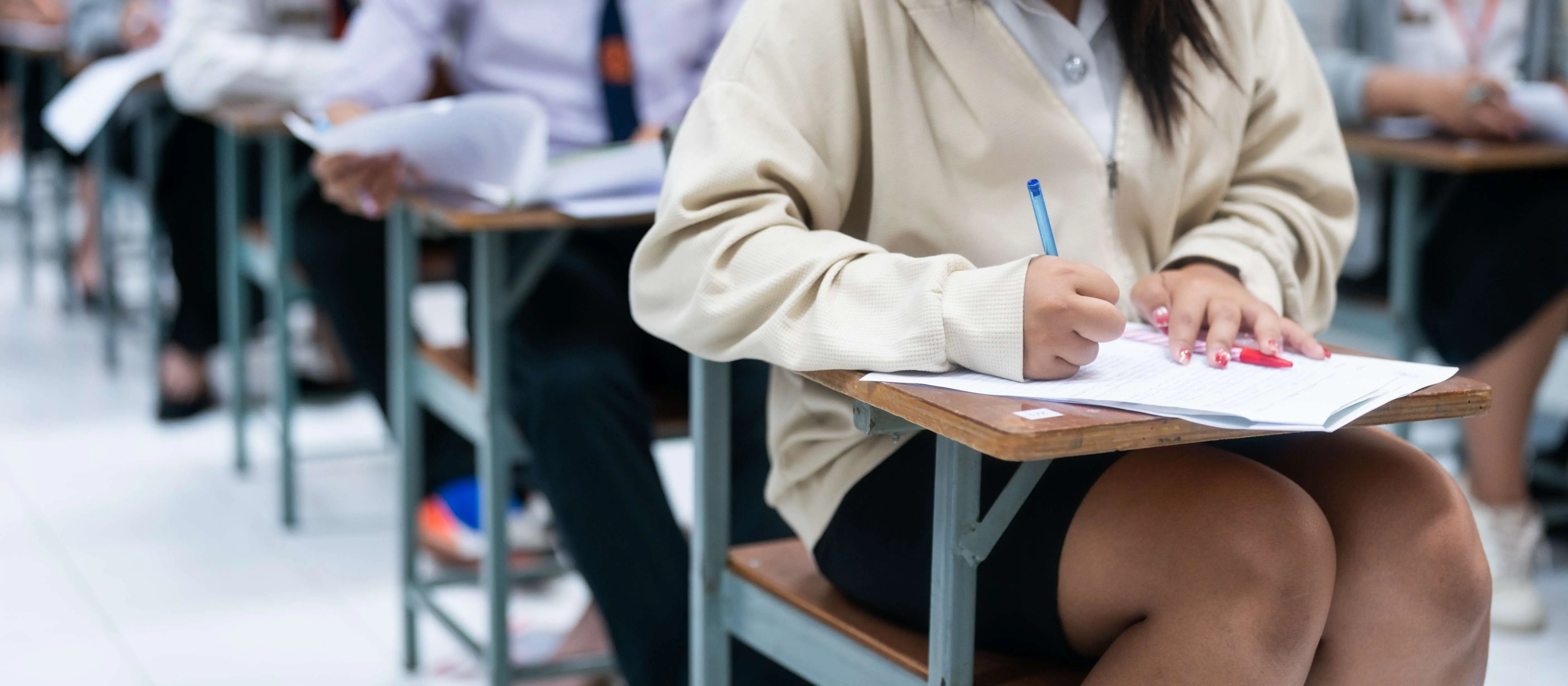 Estudantes sentados em cadeiras em uma sala de aula escrevendo.