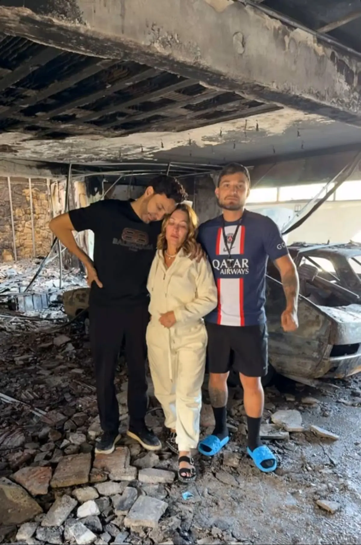 Três pessoas em foto com o que restou da casa dos pais de MC Gui após incêndio em São Paulo.