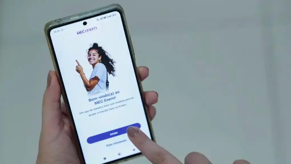 Mãos segurando celular com o app do MEC aberto para matéria sobre o prazo para pedir isenção da taxa do Enem 2026.