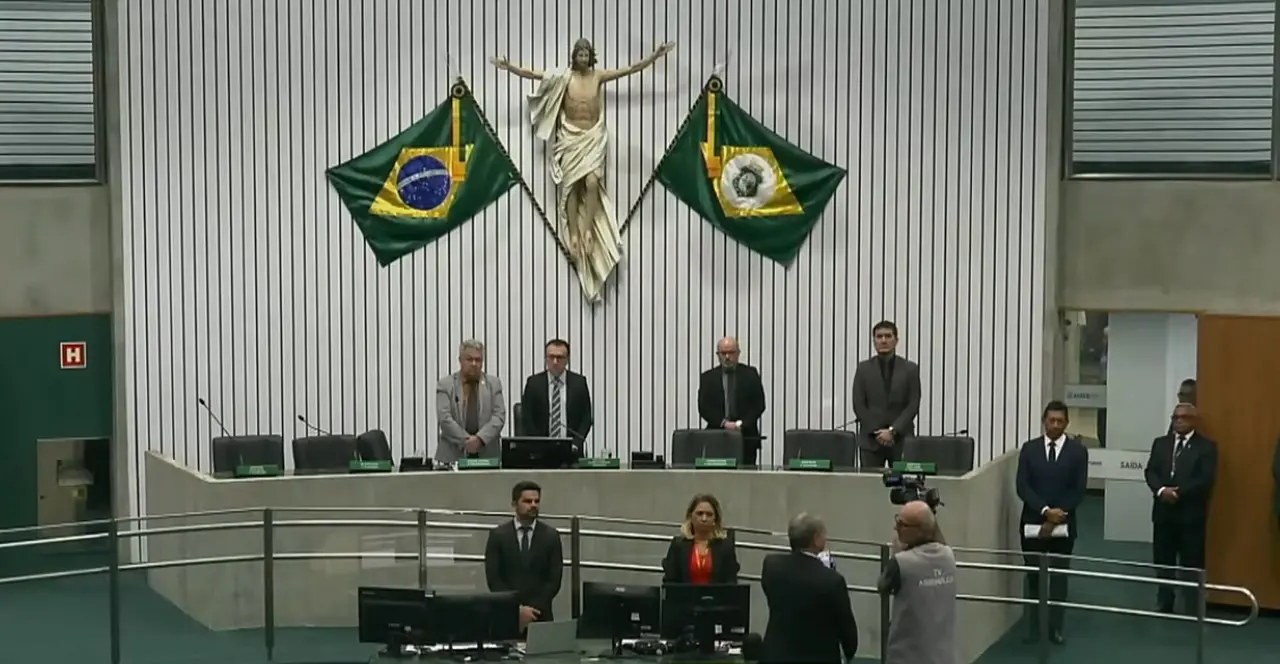 Plenário com parlamentares em pé, prestando minuto de silêncio.