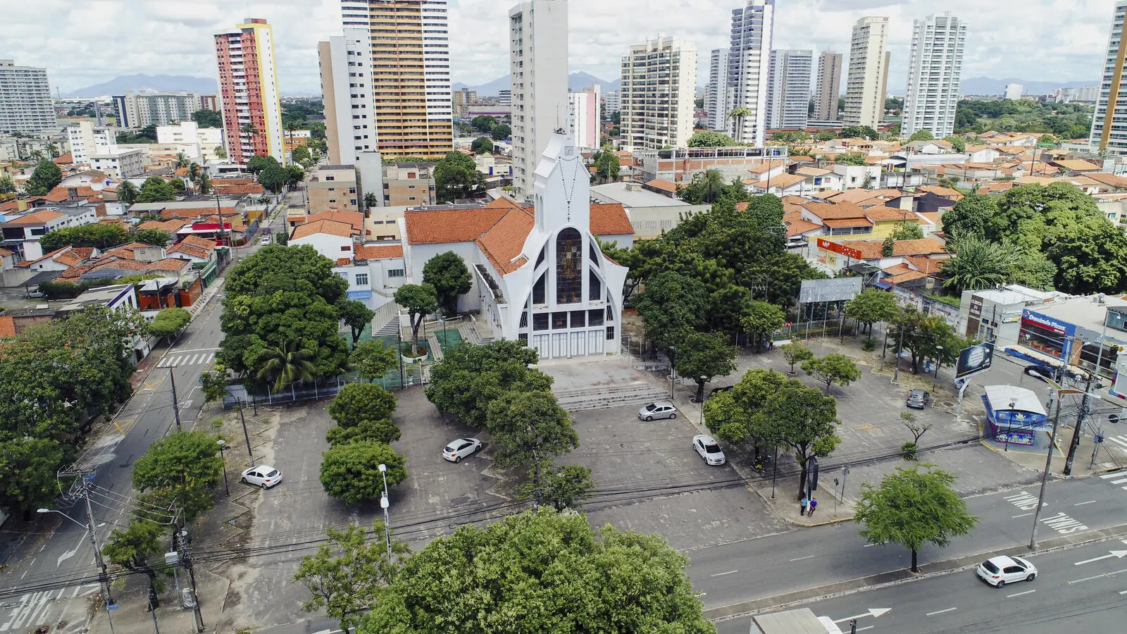 Imagem aérea da Igreja de Nossa Senhora de Fátima e sua praça arborizada, cercada por casas de telhado cerâmico e edifícios residenciais ao fundo, característicos do bairro.