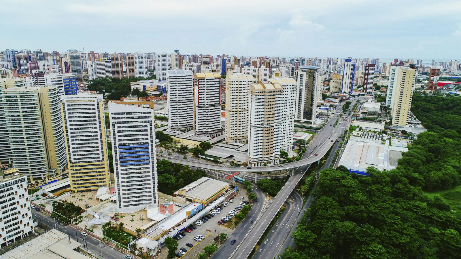 Panorama moderno do bairro Cocó, destacando a densa linha de prédios de alto padrão contornando a vasta área verde do Parque do Cocó e o viaduto da Avenida Engenheiro Santana Júnior.