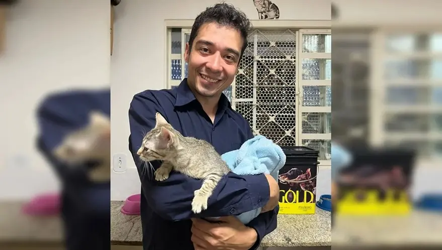 Homem feliz segurando um gato de estimação dentro de casa, ambiente com móveis e objetos de rotina diária