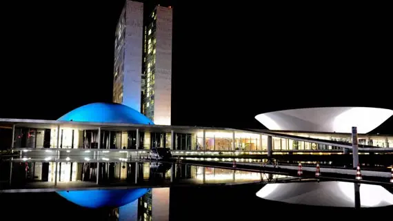 Estrutura do Congresso Nacional à noite, com luzes brancas e azuis.