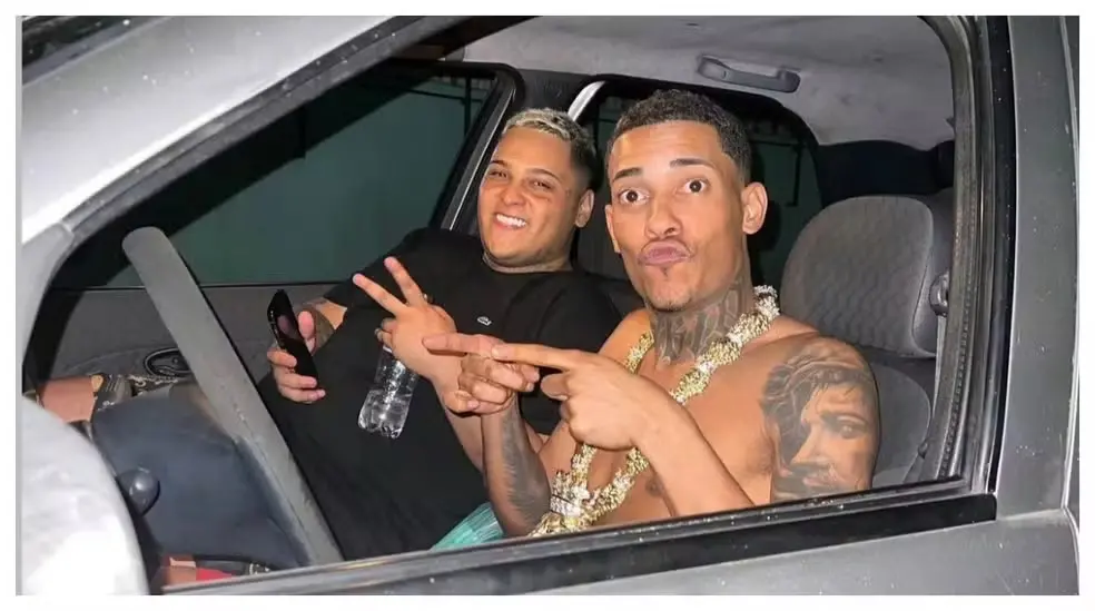 MCs Poze do Rodo e Ryan SP dentro de um carro, fazendo pose descontraída e sorrindo para a câmera em um momento de diversão. Foto capturada em ambiente fechado.