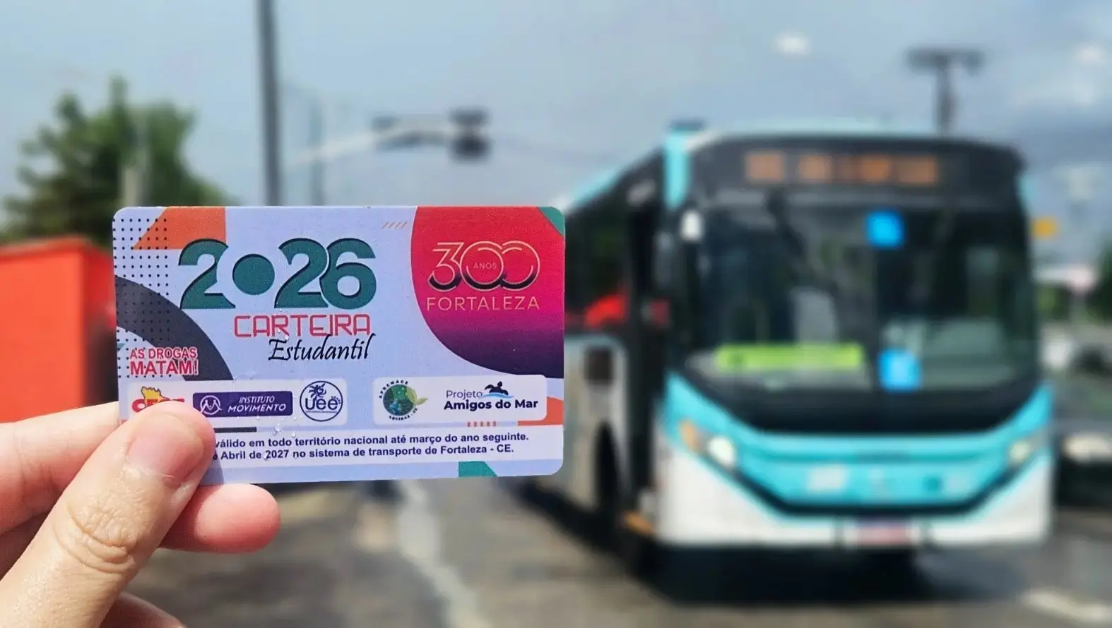 Carteira estudantil de 2026 em primeiro plano e ônibus da frota municipal ao fundo. Imagem utilizada em matéria em que informa sobre prorrogação da validade do documento.