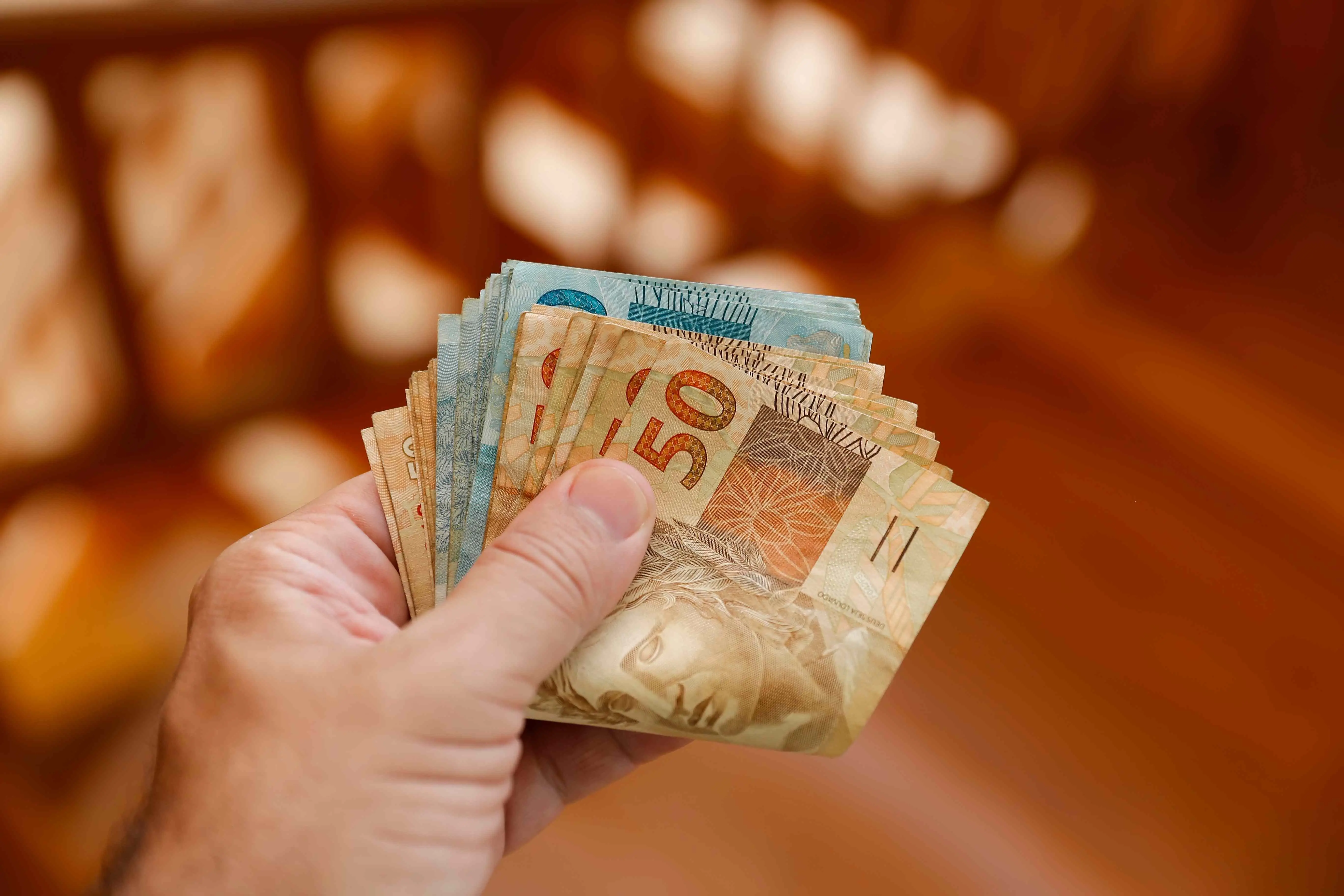 Mão segurando cédulas de real brasileiro.