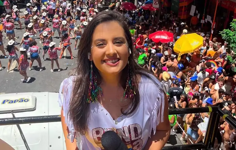 Mulher sorrindo em cima de um carro durante um grande bloco de carnaval com muitas pessoas e foliões ao fundo