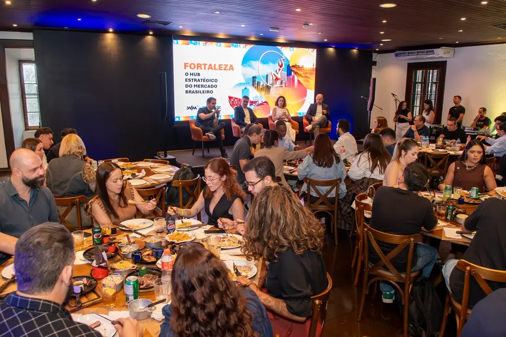 Público em mesas de restaurante acompanha painel.