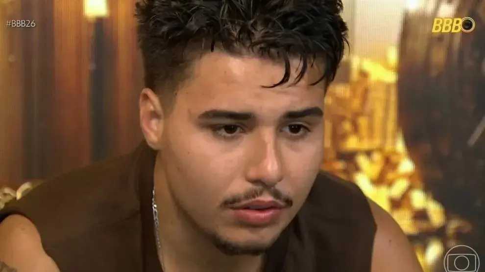 Pedro é um homem branco de cabelo preto, bigode e cavanhaque. Na foto, ele usa regata marrom e está com expressão surpresa.