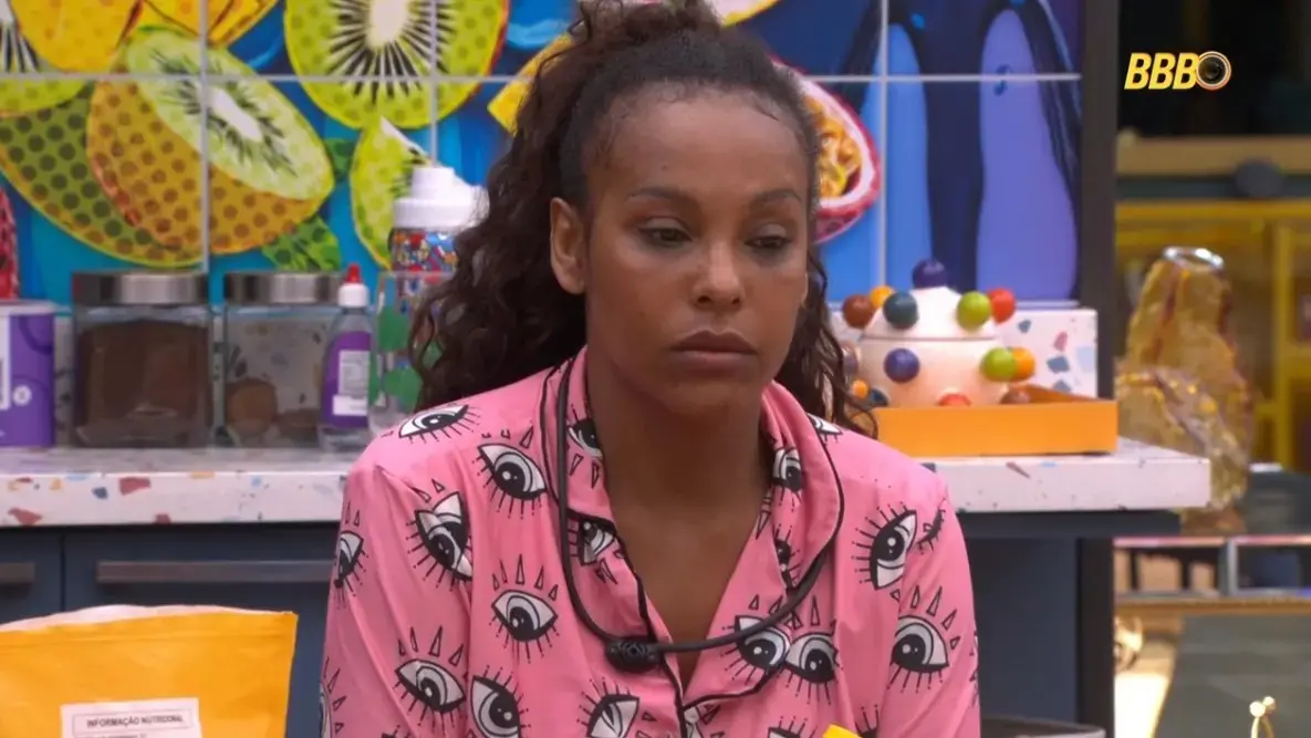 Sol Vega é uma mulher jovem negra de cabelo amarrado em um rabo de cavalo. Na foto, ela usa um pijama rosa estampado e está com expressão triste.