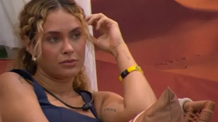 Sarah é uma mulher jovem branca e loira, de cabelo ondulado. Na foto, ela está com expressão séria.