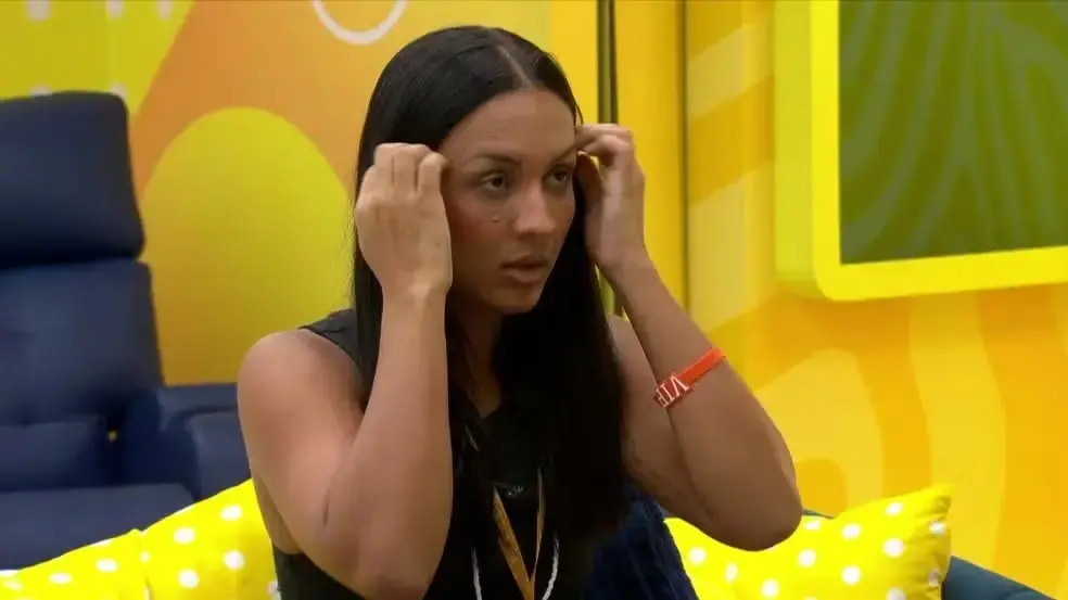 Maxiane é uma mulher negra de cabelo preto liso e longo. Na foto, ela está passando as mãos no cabelo.