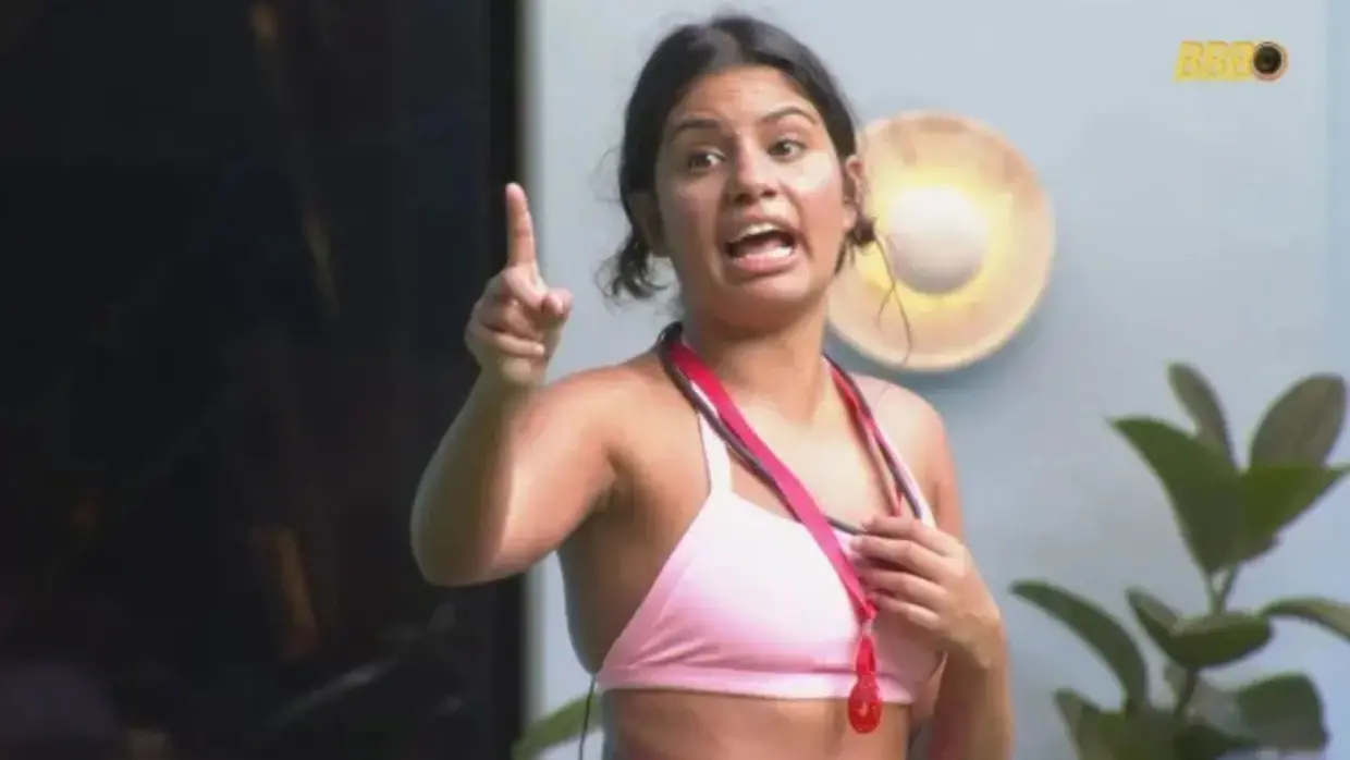 Gabriela é uma jovem negra de pele clara e cabelo liso amarrado. Na foto, ela está com o dedo indicador para o alto durante uma discussão. Usa um top rosa.