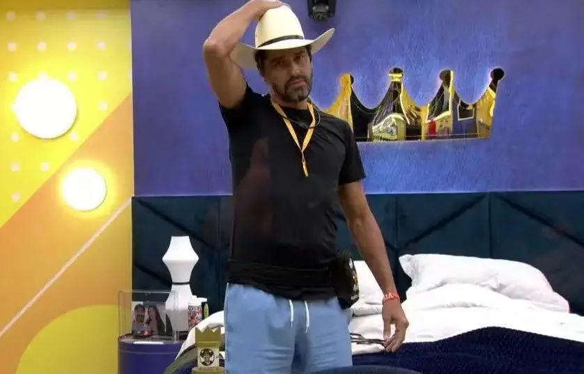 Alberto Cowboy é um homem de meia idade e, na foto, usa camisa preta, bermuda azul e chapéu branco.