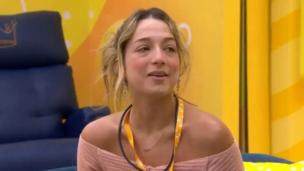 Samira é uma jovem loira, branca, de cabelo loiro amarrado em um coque. Na foto, ela está de blusa rosa e colar do Líder.