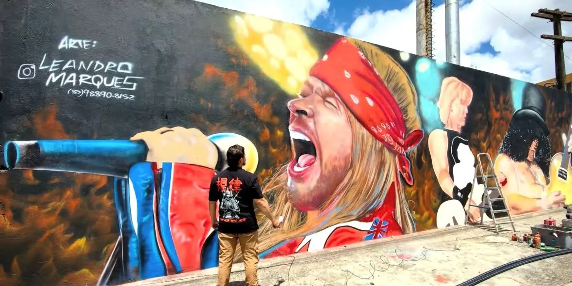 Leandro Marques, artista visual, de frente para o seu mural do Guns N' Roses, com destaque para Axl Rose.
