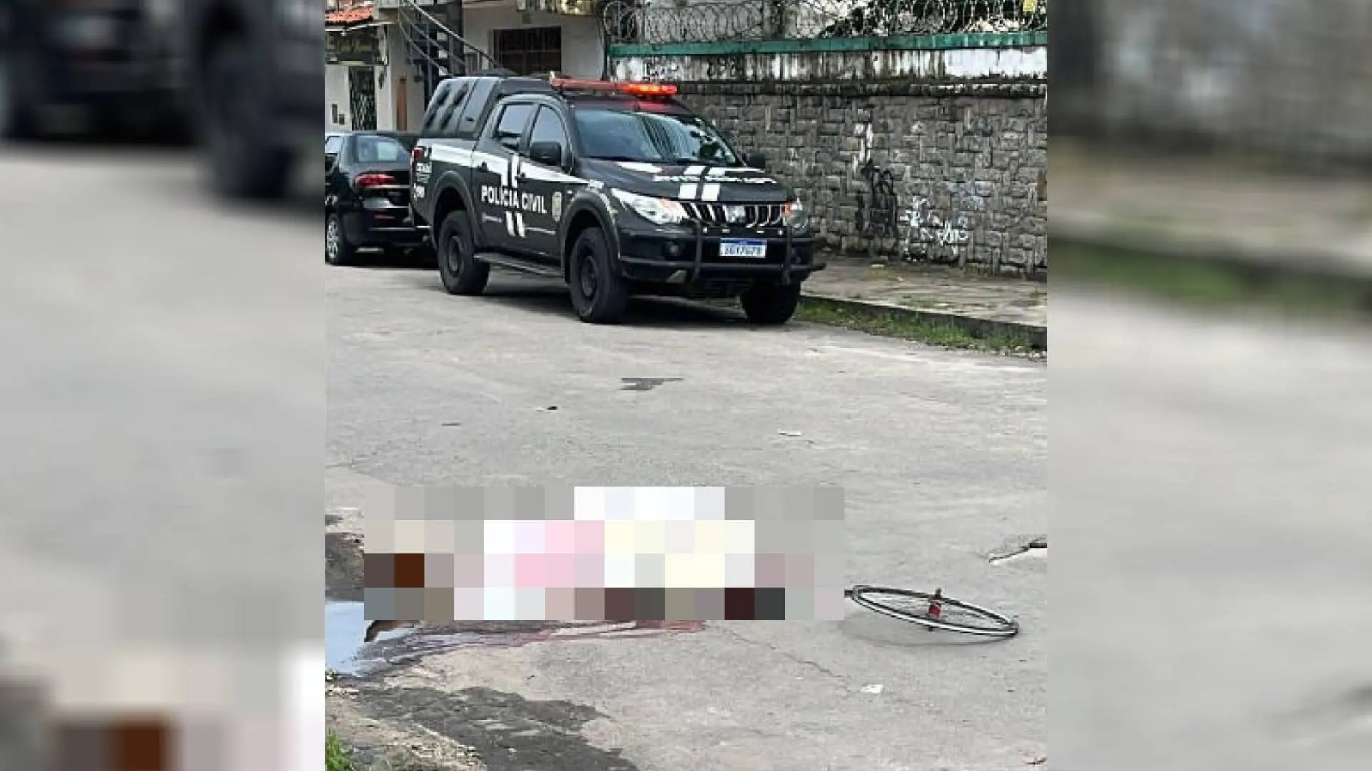 Foto que mostra corpo ensanguentado coberto por lençol e borrado por pixels. Ao fundo há uma viatura da Polícia Civil do Ceará.