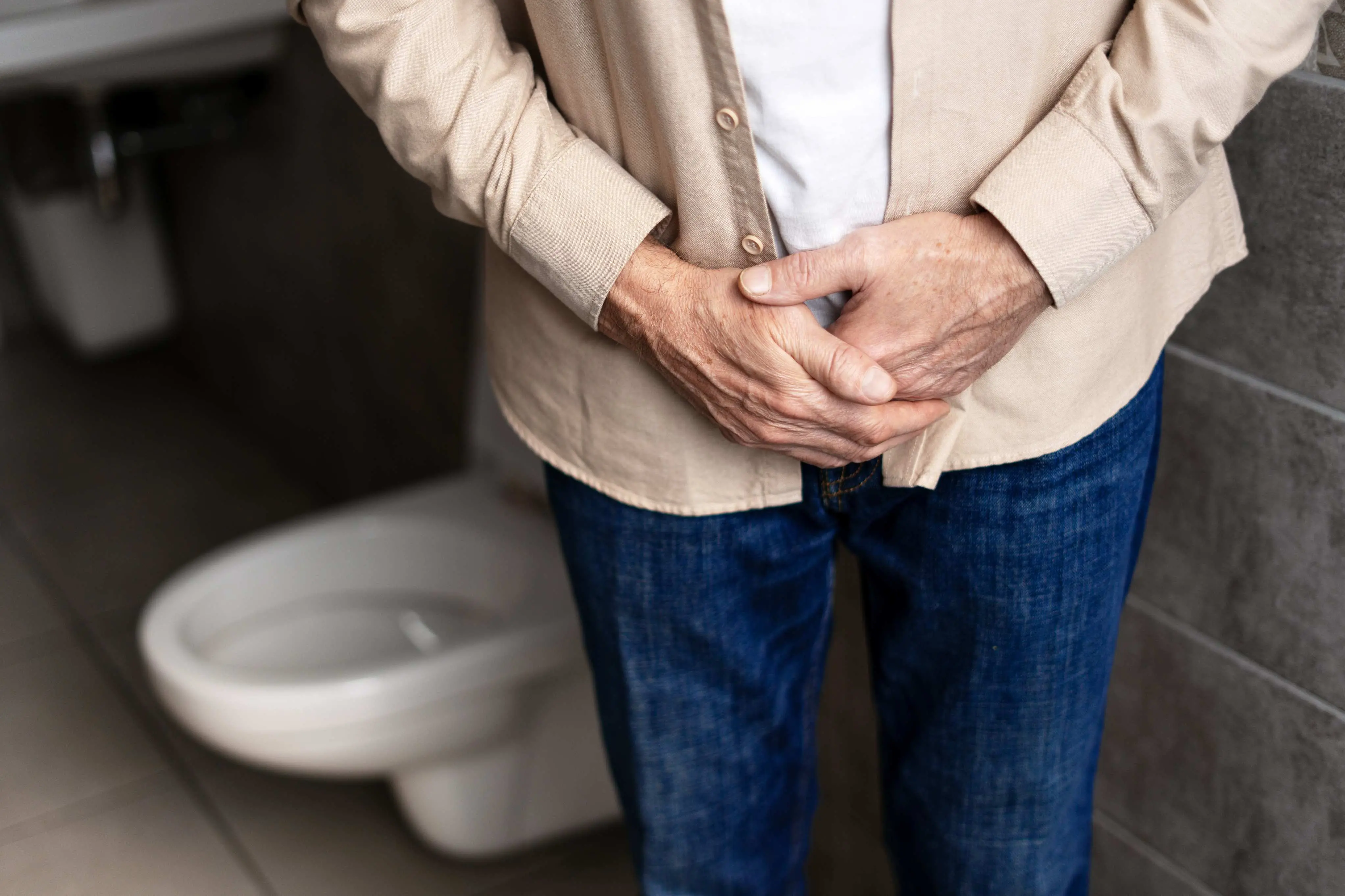 Imagem de homem com a mão na barriga, na área da bexiga, para matéria sobre entenda o que é a hiperplasia da próstata.