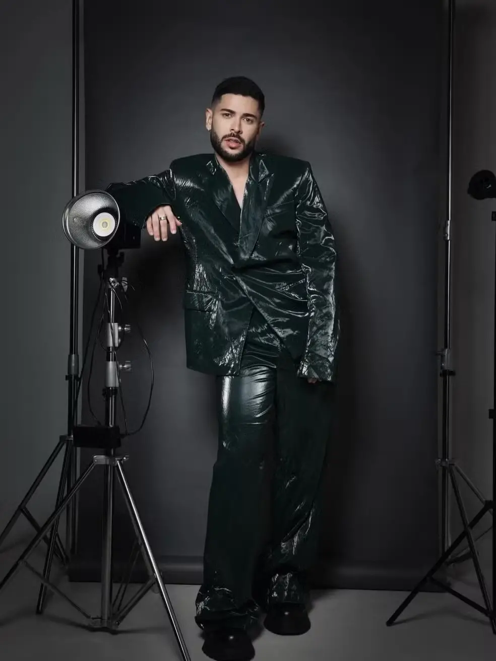 Marcelo é um homem jovem branco, de cabelo e barba curtos. Na foto, ele usa terno e calça preto brilhosos.